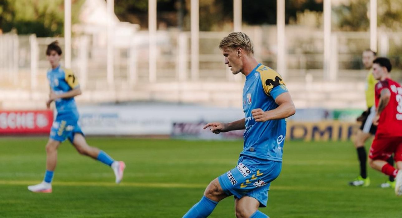 Fußballspieler im blauen Trikot mit gelben Akzenten auf einem Rasen im Stadion
